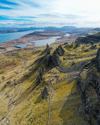 Aerial view of The Storr featuring dramatic rock formations a winding hiking trail and expansive views of the surrounding landscape and loch in Portree Scotland United Kingdom. Aerial view of The Storr featuring dramatic rock formations a winding hiking trail and expansive views of the surrounding landscape and loch in Portree Scotland United Kingdom.