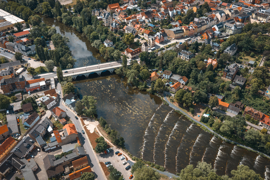Aerial view of the Saale river flowing through the historic town of Saalfeld featuring a stone bridge lush green trees and traditional rooftops in Saalfeld Thuringia Germany. Aerial view of the Saale river flowing through the historic town of Saalfeld featuring a stone bridge lush green trees and traditional rooftops in Saalfeld Thuringia Germany.