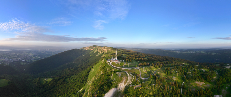 Aerial view of Col de la Faucille featuring a prominent communications tower lush green mountain slopes dense pine forests and winding roads in Gex Auvergne Rhone Alpes France.
