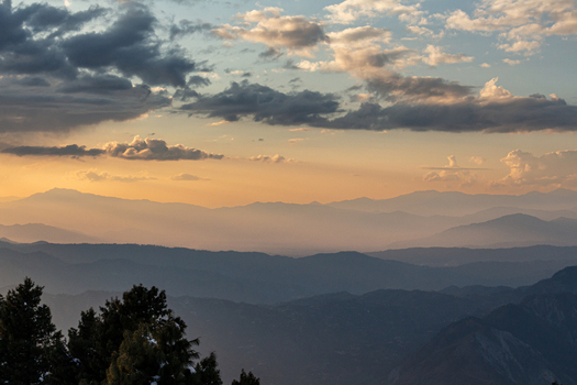 View of hazy mountain ranges fading into the horizon under a sky streaked with golden light and dramatic clouds Arang Kel Azad Kashmir Pakistan.