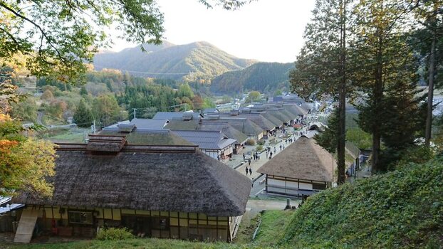 View of Ouchi juku with traditional thatched roof houses lining the historic street surrounded by lush autumn mountains in Shimogo Fukushima Japan.