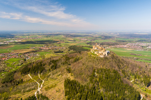 Burg Hohenzollern Germany 27 September 2026 Aerial view of Hohenzollern Castle perched on a hilltop surrounded by lush forests and rolling green fields under a clear blue sky.