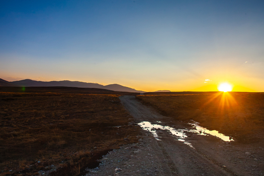View of the Deosai National Park landscape at sunset with a dirt road and puddles reflecting the golden light in Astore Gilgit Pakistan. View of the Deosai National Park landscape at sunset with a dirt road and puddles reflecting the golden light in Astore Gilgit Pakistan.