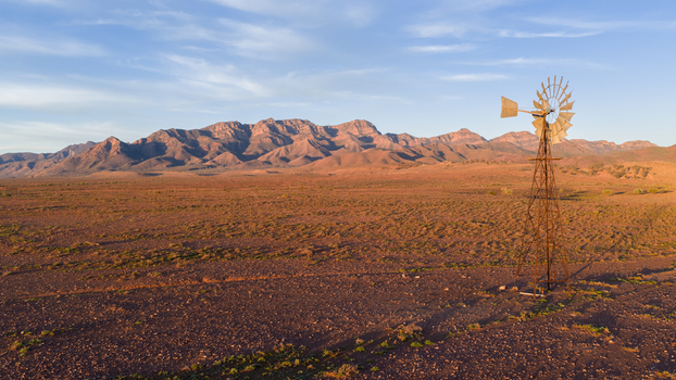 Aerial view of a traditional windmill standing in the arid outback landscape with rugged mountain peaks under a clear sky Flinders Ranges South Australia Australia. Aerial view of a traditional windmill standing in the arid outback landscape with rugged mountain peaks under a clear sky Flinders Ranges South Australia Australia.