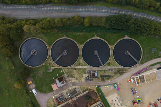 Aerial view of a wastewater treatment plant with four large circular sedimentation tanks surrounded by green fields and a railway line in the United Kingdom. Aerial view of a wastewater treatment plant with four large circular sedimentation tanks surrounded by green fields and a railway line in the United Kingdom.