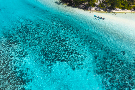 View of a tropical beach with turquoise water a coral reef a small outrigger boat and people on the white sand shore in Moorea Maiao Windward Islands French Polynesia.