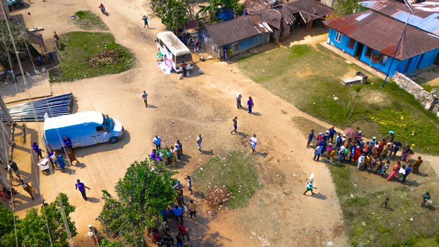 Aerial view of a community gathering with a white van and a small bus parked on a dirt road surrounded by houses with metal roofs and groups of people in Abua Rivers Nigeria. Aerial view of a community gathering with a white van and a small bus parked on a dirt road surrounded by houses with metal roofs and groups of people in Abua Rivers Nigeria.