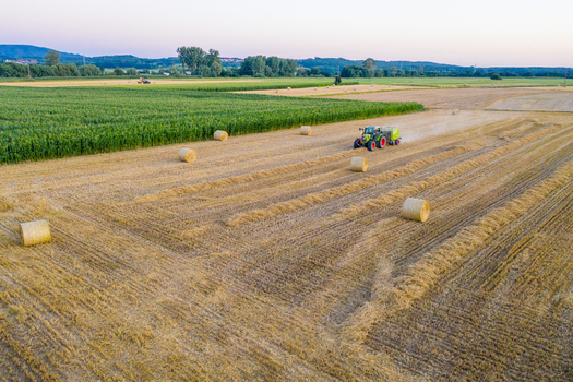 Aerial view of a tractor baling hay in the Knoblauchsland region with round straw bales and green fields Nuremberg Bavaria Germany. Aerial view of a tractor baling hay in the Knoblauchsland region with round straw bales and green fields Nuremberg Bavaria Germany.