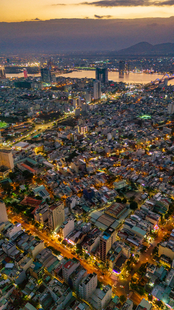 Aerial view of the illuminated cityscape of Da Nang at dusk featuring dense urban architecture glowing street lights and the Han River in Da Nang Vietnam. Aerial view of the illuminated cityscape of Da Nang at dusk featuring dense urban architecture glowing street lights and the Han River in Da Nang Vietnam.