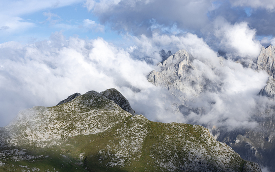 View of rugged peaks piercing through a sea of ethereal clouds contrasting with the verdant slopes below Picos de Europa National Park Picos de Europa Asturias Spain. View of rugged peaks piercing through a sea of ethereal clouds contrasting with the verdant slopes below Picos de Europa National Park Picos de Europa Asturias Spain.