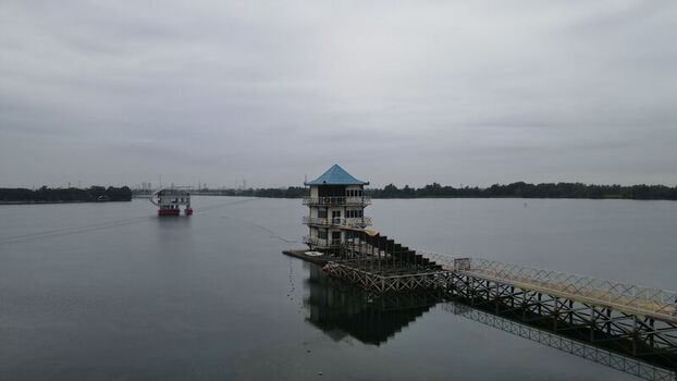 Aerial view of the Jakabaring Sport City lake featuring a building with a blue roof and wooden pier surrounded by calm water in Kecamatan Seberang Ulu I Sumatera Selatan Indonesia. Aerial view of the Jakabaring Sport City lake featuring a building with a blue roof and wooden pier surrounded by calm water in Kecamatan Seberang Ulu I Sumatera Selatan Indonesia.