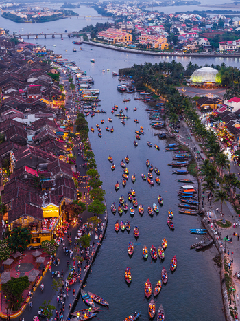 Aerial view of the Thu Bon River featuring numerous small wooden boats illuminated historic buildings and bustling waterfront streets at dusk in Hoi An Vietnam. Aerial view of the Thu Bon River featuring numerous small wooden boats illuminated historic buildings and bustling waterfront streets at dusk in Hoi An Vietnam.