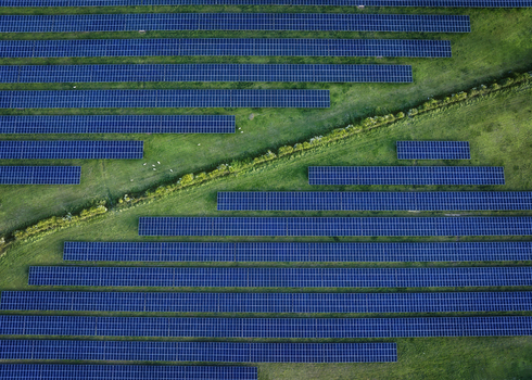 Aerial view of Gillinstown Solar Farm with rows of blue photovoltaic panels installed on lush green fields divided by a natural hedge in County Meath Ireland.