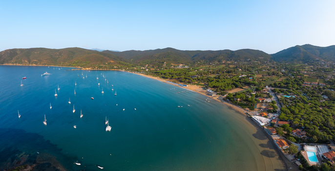 Aerial view of Lacona Beach with anchored sailboats on the turquoise water sandy coastline and lush green hills in Lacona Tuscany Italy.