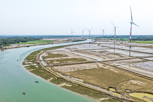 Aerial view of wind turbines standing tall against the pale sky contrasting with the winding river and textured land Cox s Bazar Chittagong Division Bangladesh. Aerial view of wind turbines standing tall against the pale sky contrasting with the winding river and textured land Cox s Bazar Chittagong Division Bangladesh.