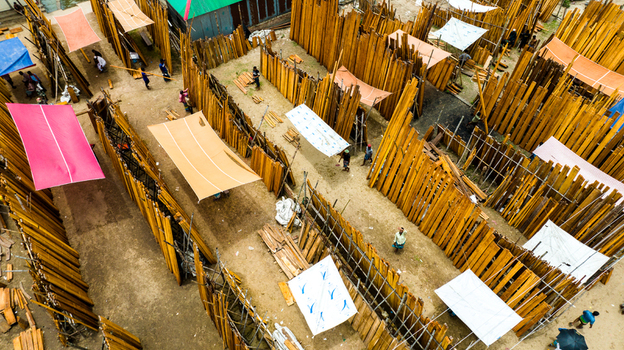 Aerial view of Baish Mowza Sarak Bazar featuring rows of stacked lumber and colorful fabric canopies with people walking through the market in Nabinagar Chittagong Division Bangladesh. Aerial view of Baish Mowza Sarak Bazar featuring rows of stacked lumber and colorful fabric canopies with people walking through the market in Nabinagar Chittagong Division Bangladesh.