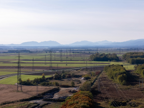 Aerial view of high voltage power lines crossing agricultural fields and green forests with mountains in the background in Slovenia. Aerial view of high voltage power lines crossing agricultural fields and green forests with mountains in the background in Slovenia.