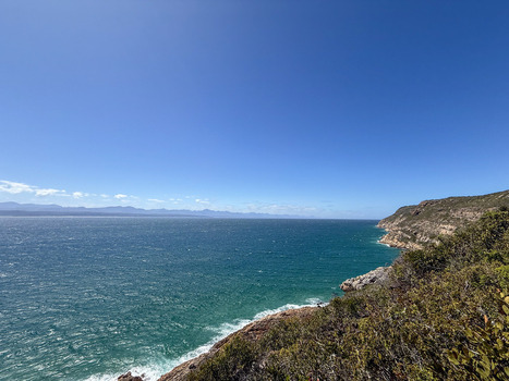 View of the turquoise ocean waves crashing against rocky cliffs and lush green vegetation in Plettenberg Bay Western Cape South Africa. View of the turquoise ocean waves crashing against rocky cliffs and lush green vegetation in Plettenberg Bay Western Cape South Africa.
