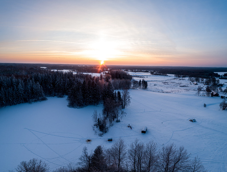 Aerial view of a snow covered landscape with dense pine forests and open fields at sunset in Latvia. Aerial view of a snow covered landscape with dense pine forests and open fields at sunset in Latvia.