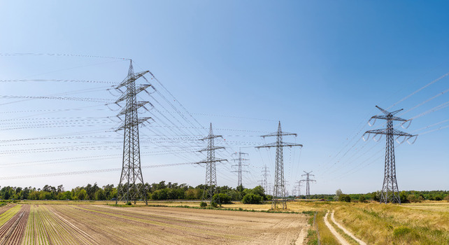 Aerial view of the Amprion Umspannwerk power transmission lines stretching across agricultural fields under a clear blue sky in Pfungstadt Hessen Germany.