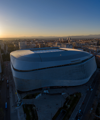 Aerial view of Santiago Bernabeu stadium featuring its modern metallic facade during golden hour with the city of Madrid in the background Madrid Community of Madrid Spain. Aerial view of Santiago Bernabeu stadium featuring its modern metallic facade during golden hour with the city of Madrid in the background Madrid Community of Madrid Spain.