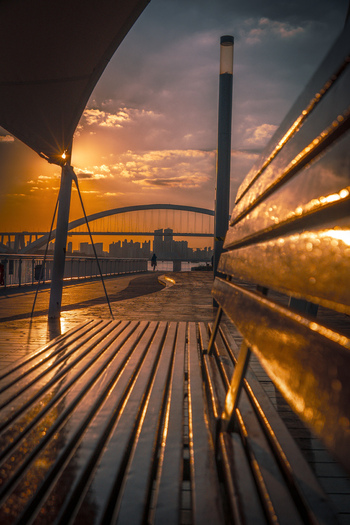 View of West Bund waterfront promenade with a wooden bench in the foreground and a bridge silhouette against the sunset sky in Shanghai Shanghai China.