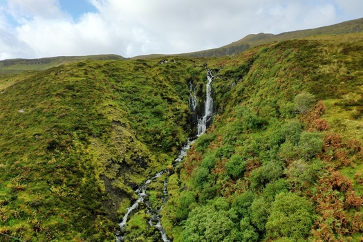Aerial view of Bride s Veil Falls cascading down a lush green hillside with rocky terrain and vegetation in Portree Scotland United Kingdom. Aerial view of Bride s Veil Falls cascading down a lush green hillside with rocky terrain and vegetation in Portree Scotland United Kingdom.