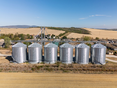 Aerial view of grain silos and agricultural storage facility in Paszto Nograd County Hungary surrounded by summer farmland and crop fields under a clear sky. Aerial view of grain silos and agricultural storage facility in Paszto Nograd County Hungary surrounded by summer farmland and crop fields under a clear sky.