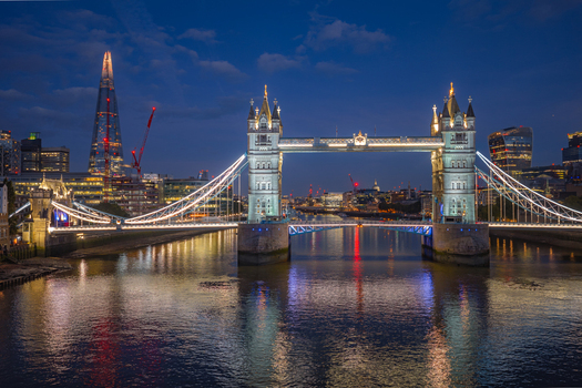 Aerial view of Tower Bridge illuminated at night with the Shard and the City of London skyline reflecting on the River Thames in London England United Kingdom.