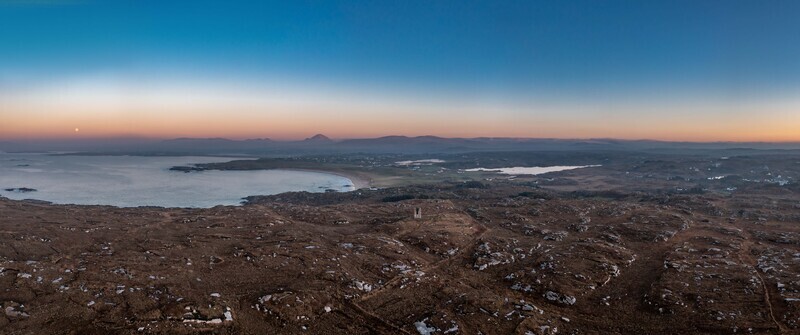 Aerial view of the rugged coastal landscape of Kincasslagh at twilight featuring rocky terrain a calm bay and distant mountains in Kincasslagh County Donegal Ireland. Aerial view of the rugged coastal landscape of Kincasslagh at twilight featuring rocky terrain a calm bay and distant mountains in Kincasslagh County Donegal Ireland.