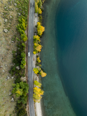Aerial view of the road winding along the tranquil lake where the azure waters meet the golden hued trees Glendhu Bay Otago Region New Zealand. Aerial view of the road winding along the tranquil lake where the azure waters meet the golden hued trees Glendhu Bay Otago Region New Zealand.