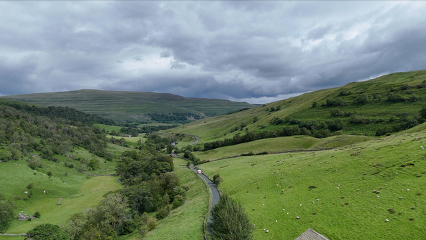 United Kingdom Yorkshire Aerial view of a lush green valley with a winding road stone walls and sheep grazing on the hillsides under a cloudy sky. United Kingdom Yorkshire Aerial view of a lush green valley with a winding road stone walls and sheep grazing on the hillsides under a cloudy sky.