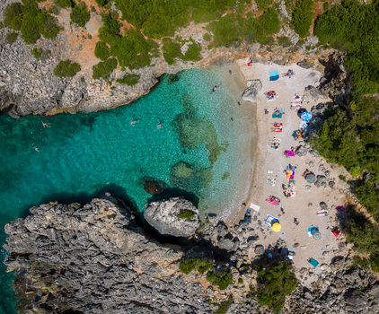 Aerial view of Aquarium Beach with turquoise water rocky cliffs people sunbathing on the sand and swimmers in the sea Jala Vlore County Albania.