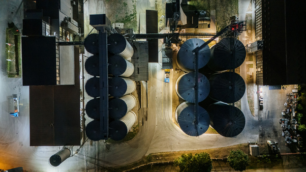 Aerial view of the grain silo facility at night featuring illuminated cylindrical storage tanks industrial structures and paved grounds in Sremska Mitrovica Vojvodina Serbia.