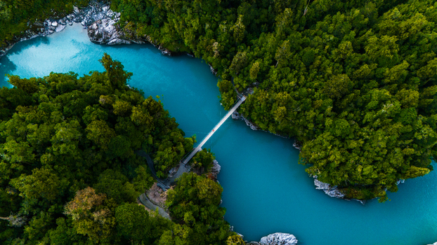 Aerial view of a milky turquoise river snaking through a dense vibrant green forest crossed by a narrow bridge Hokitika Gorge Kokatahi West Coast Region New Zealand. Aerial view of a milky turquoise river snaking through a dense vibrant green forest crossed by a narrow bridge Hokitika Gorge Kokatahi West Coast Region New Zealand.