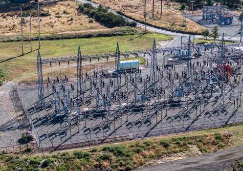 Aerial view of an electrical substation with metal structures power lines and transformers surrounded by a fence and grassy terrain in Bandon Oregon United States. Aerial view of an electrical substation with metal structures power lines and transformers surrounded by a fence and grassy terrain in Bandon Oregon United States.