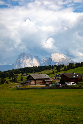 View of the Dolomites mountains rising above traditional wooden mountain houses and lush green meadows in Rocca Pietore Veneto Italy. View of the Dolomites mountains rising above traditional wooden mountain houses and lush green meadows in Rocca Pietore Veneto Italy.