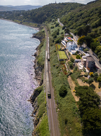 Aerial view of a train traveling along the coastal tracks in Dalkey with lush green hills and the Irish Sea in Dublin County Dublin Ireland. Aerial view of a train traveling along the coastal tracks in Dalkey with lush green hills and the Irish Sea in Dublin County Dublin Ireland.