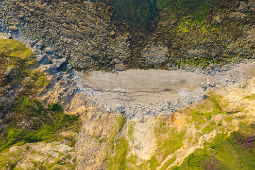 Aerial view of a rugged coastal cove featuring rocky cliffs a small pebble beach and vibrant green vegetation in Camborne England United Kingdom.