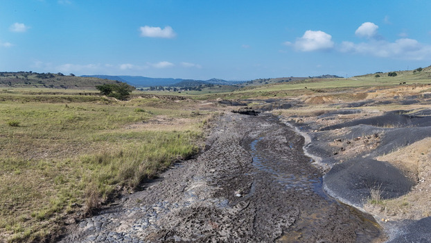 Aerial view of a dark industrial runoff area cutting through green rolling hills and rural landscape under a blue sky Pietermaritzburg KwaZulu Natal South Africa.