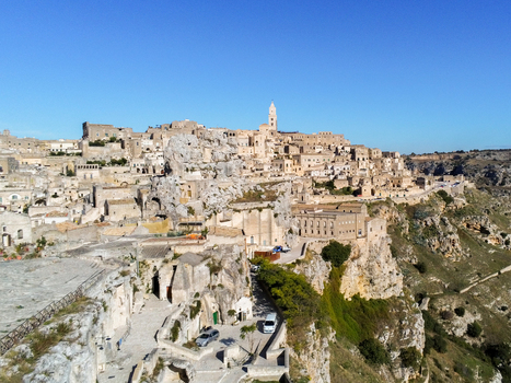 Aerial view of the historic Sassi di Matera with ancient stone buildings carved into the cliffside under a clear blue sky in Matera Basilicata Italy.