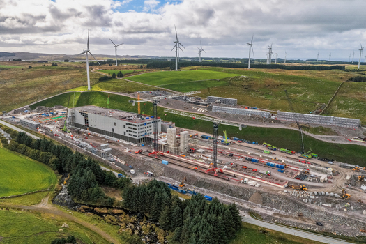 Aerial view of the Green Mountain data center construction site featuring large industrial buildings tall cranes and surrounding wind turbines on green hills in Undheim Rogaland Norway. Aerial view of the Green Mountain data center construction site featuring large industrial buildings tall cranes and surrounding wind turbines on green hills in Undheim Rogaland Norway.