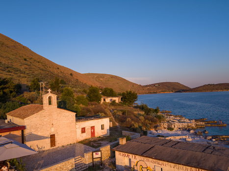 Aerial view of the small stone St. Nicholas Church on the rocky coast of Porto Palermo Bay with rolling hills and blue sky in Porto Palermo Qarku i Vlores Albania. Aerial view of the small stone St. Nicholas Church on the rocky coast of Porto Palermo Bay with rolling hills and blue sky in Porto Palermo Qarku i Vlores Albania.