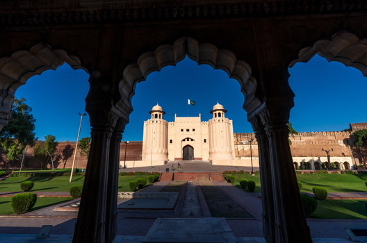 View of Lahore Fort framed by historic arched architecture with manicured lawns and clear blue sky in Lahore Punjab Pakistan.