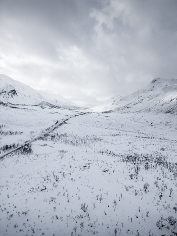 Aerial view of a vast snow covered valley with a winding road between high mountains under an overcast sky Ersfjord Troms Norway. Aerial view of a vast snow covered valley with a winding road between high mountains under an overcast sky Ersfjord Troms Norway.