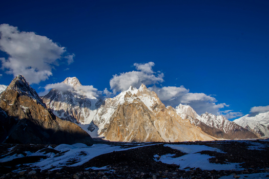 View of the snow capped peaks of Gasherbrum IV and the Karakoram range under a clear blue sky with scattered clouds in Skardu Gilgit Pakistan. View of the snow capped peaks of Gasherbrum IV and the Karakoram range under a clear blue sky with scattered clouds in Skardu Gilgit Pakistan.