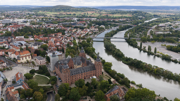 Aerial view of Schloss Johannisburg situated on the banks of the Main river surrounded by historic town rooftops and lush greenery in Aschaffenburg Bayern Germany.