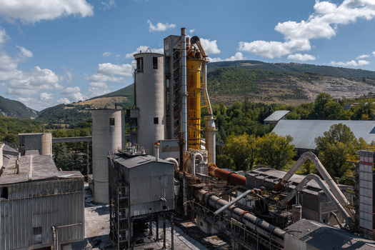Aerial view of the Sacci S.P.A. cement plant featuring large concrete silos industrial metal piping and processing structures nestled among green hills in Castelraimondo Marche Italy. Aerial view of the Sacci S.P.A. cement plant featuring large concrete silos industrial metal piping and processing structures nestled among green hills in Castelraimondo Marche Italy.
