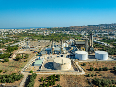Aerial view of the power plant facility with large storage tanks and industrial chimneys surrounded by olive groves and the urban landscape of Chania Greece.