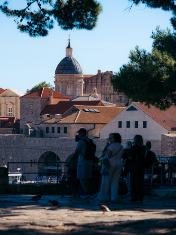 View of the historic Dubrovnik Old Town with the Cathedral dome and red tiled rooftops seen behind people in the shade in Dubrovnik Dubrovnik Neretva County Croatia. View of the historic Dubrovnik Old Town with the Cathedral dome and red tiled rooftops seen behind people in the shade in Dubrovnik Dubrovnik Neretva County Croatia.